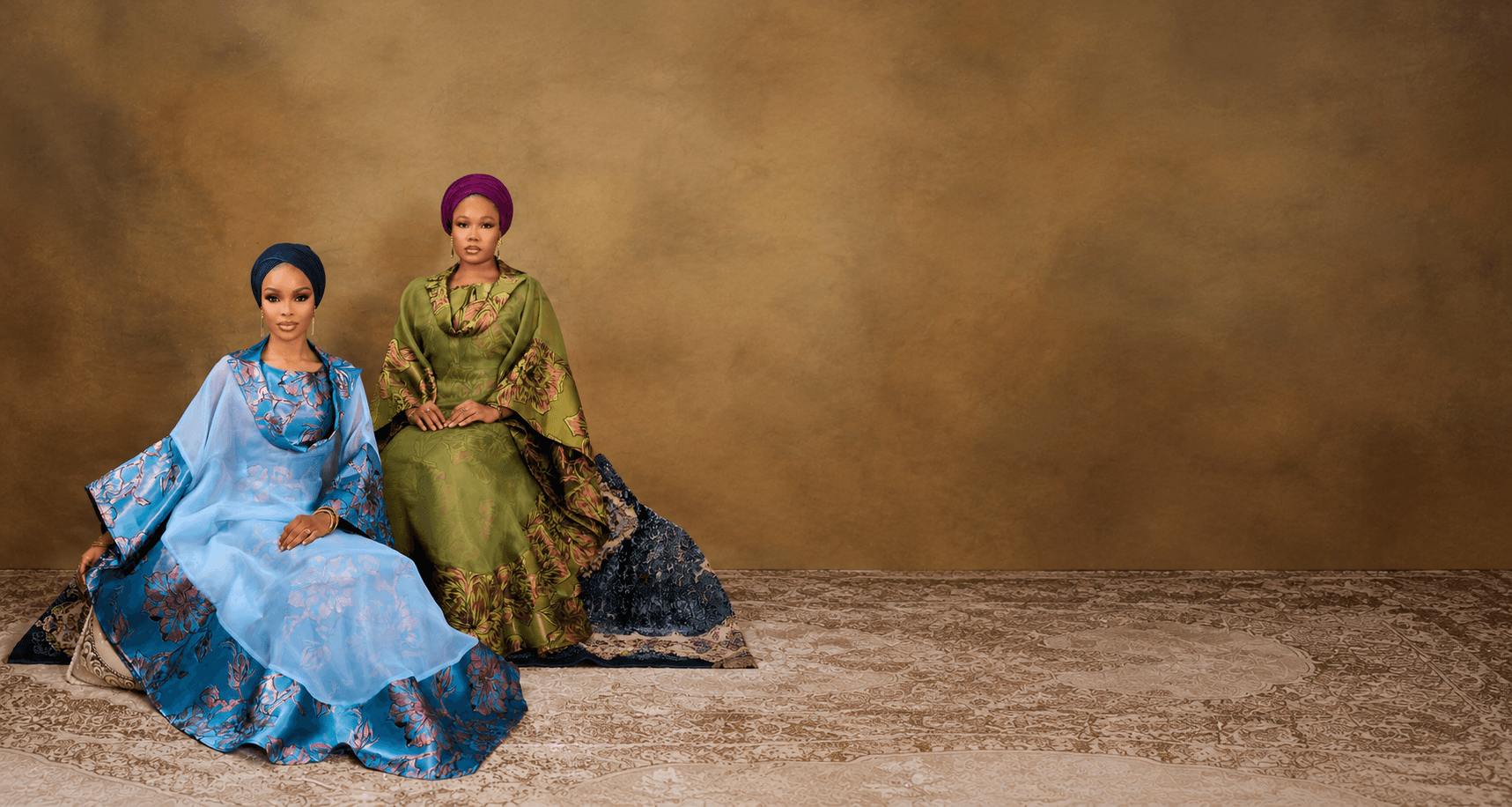 models in elegant blue floral and olive green gowns with vibrant headwraps against a warm, earthy studio backdrop
